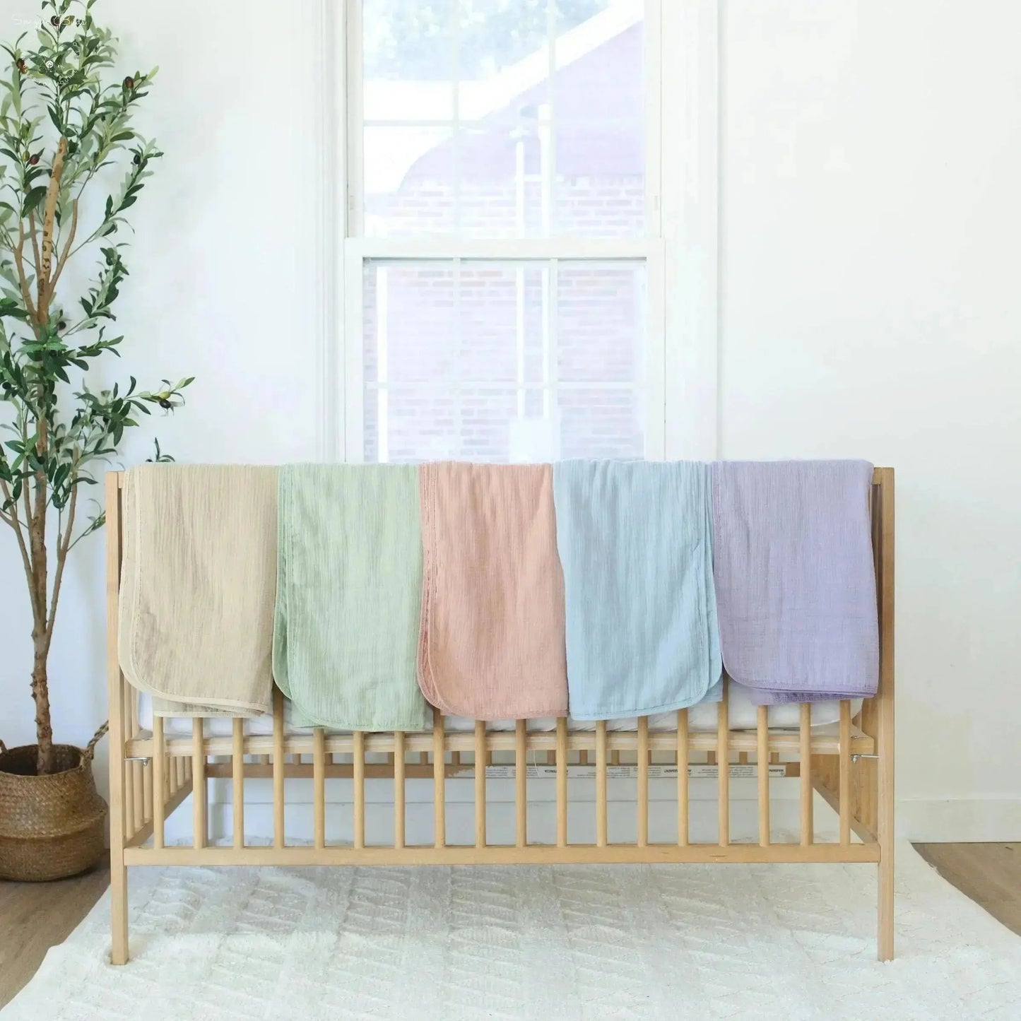Wooden crib with colorful blankets in a room with a plant and window.