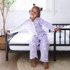 Child in purple butterfly pajamas sitting on a black crib in a bright room.