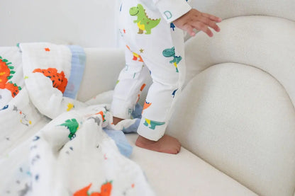 Child in dinosaur-themed pajamas standing on a white couch with colorful dinosaur blankets.