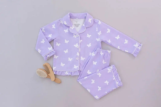 Child in purple butterfly pajamas sitting on a black crib in a bright room.