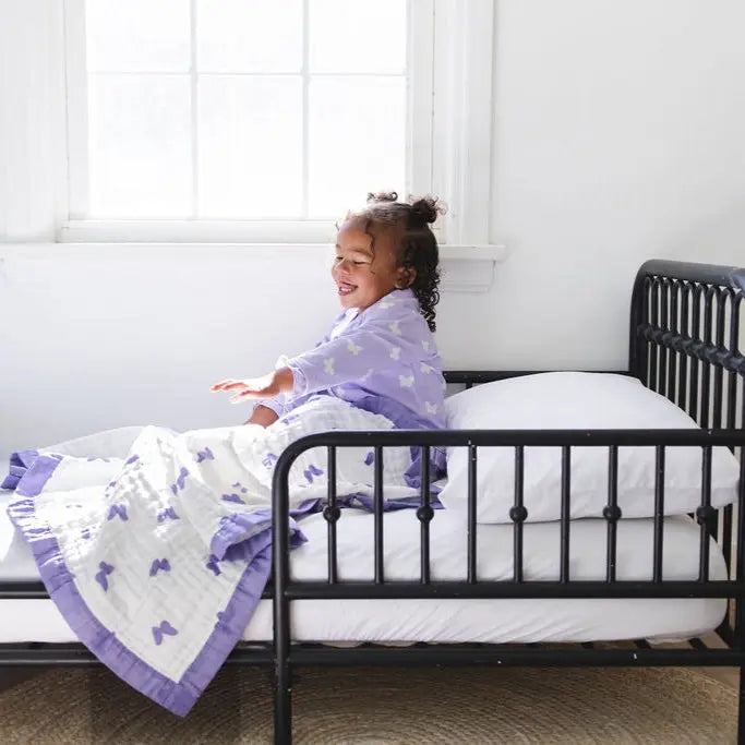 Child sitting on a bed with a purple blanket in a bright room