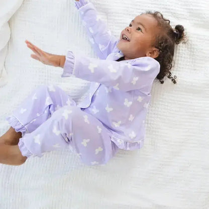 Child in purple butterfly pajamas lying on a white bed