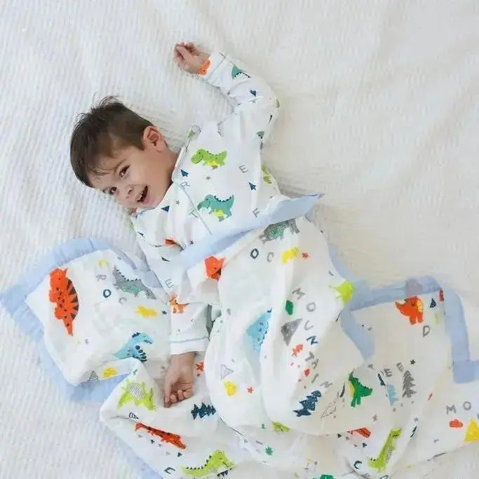 Child lying on a white blanket with a colorful dinosaur-patterned blanket