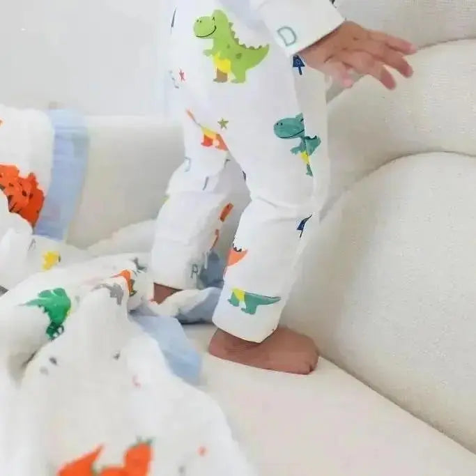 Child in dinosaur-themed pajamas standing on a white couch with colorful dinosaur blankets.