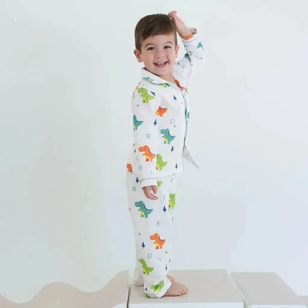 Child wearing dinosaur-themed pajamas standing on a white platform with a plain background