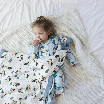 Child wrapped in a penguin-patterned blanket on a white bed