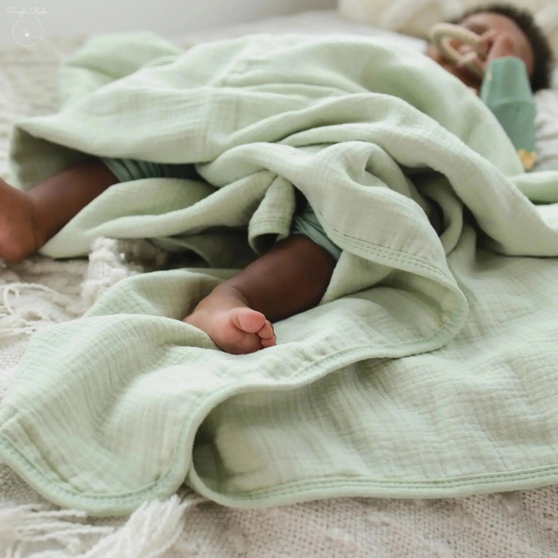 Baby wrapped in a light green blanket on a textured surface