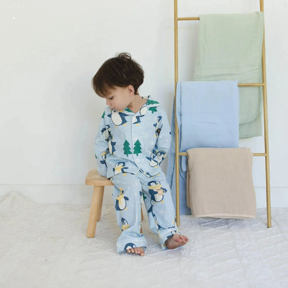 Child in penguin pajamas sitting on a stool next to a ladder with folded blankets.