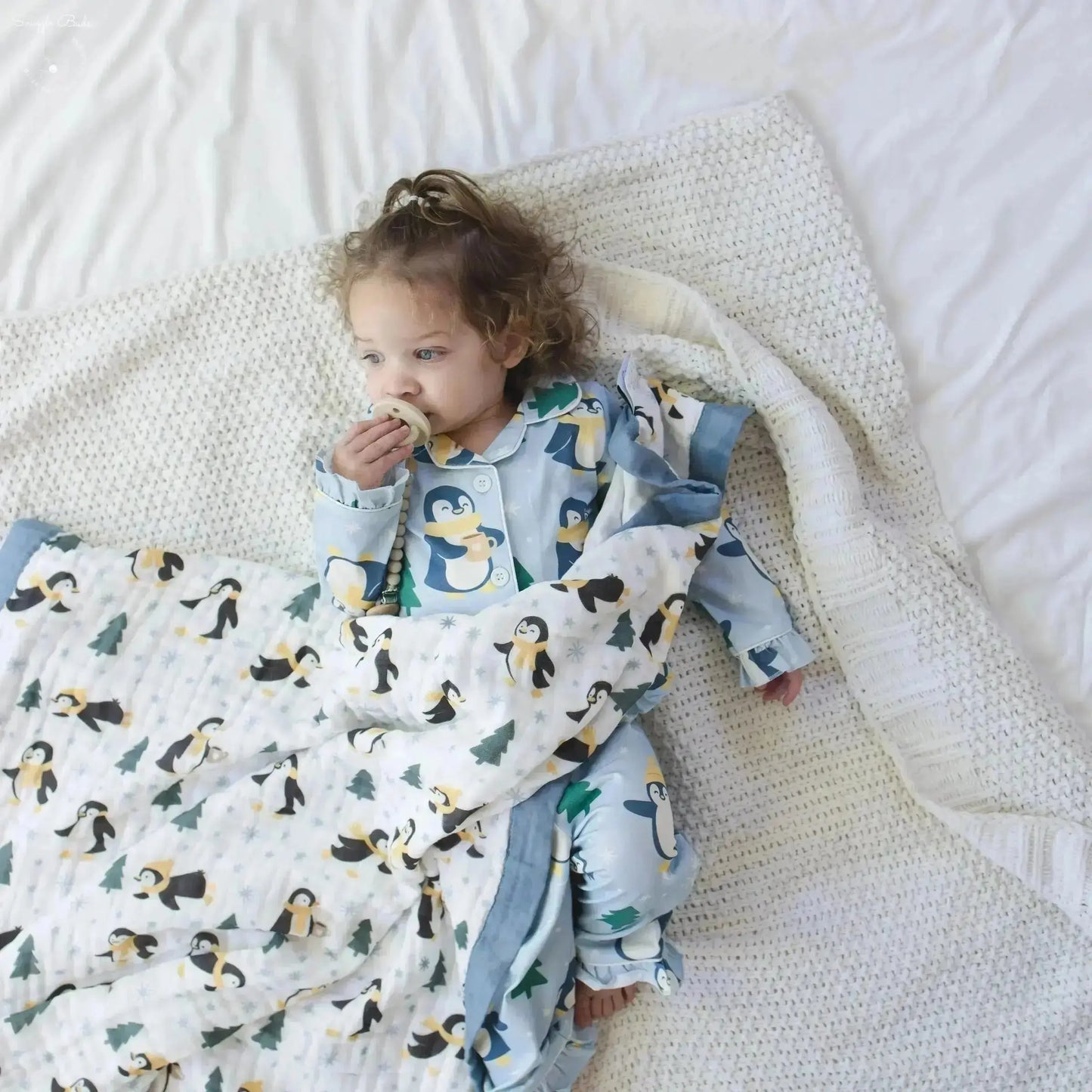 Child wrapped in a penguin-patterned blanket on a white bed