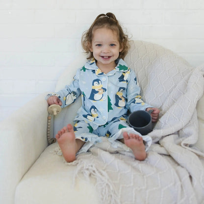 Child in a penguin-themed onesie sitting on a white couch with a blanket.