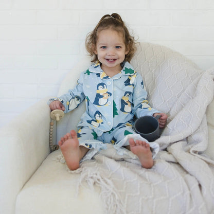 Child in a penguin-themed onesie sitting on a white couch with a blanket.
