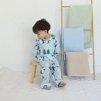 Child in penguin pajamas sitting on a stool next to a ladder with folded blankets.